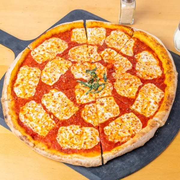 A sliced Margherita pizza with fresh mozzarella, red sauce, and basil on a dark pizza peel.