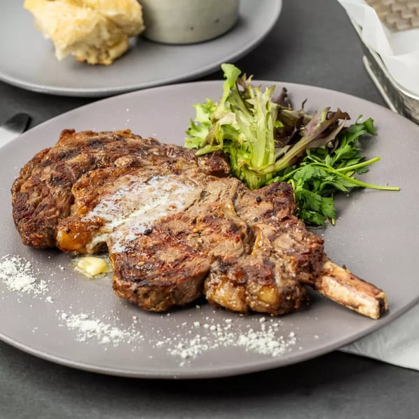 Grilled steak with melted butter, fresh greens, and sprinkled parmesan on a gray plate.