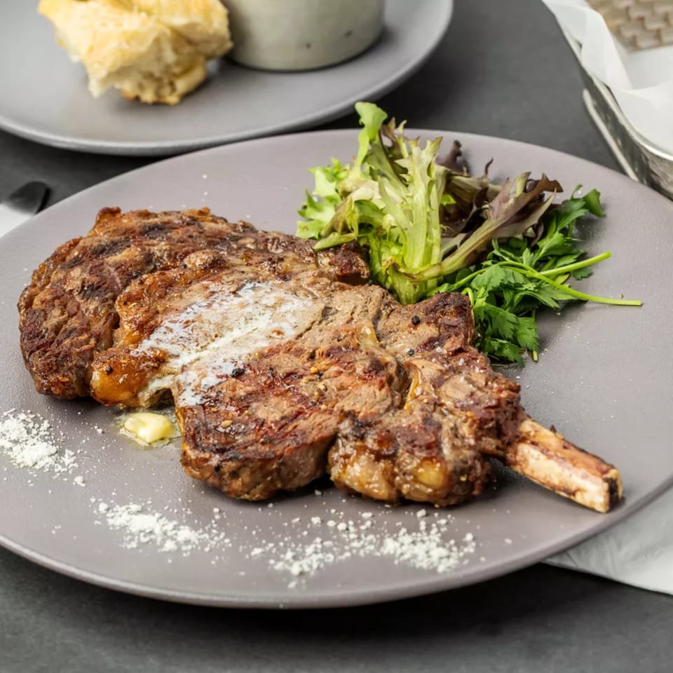 Grilled steak with melted butter, fresh greens, and sprinkled parmesan on a gray plate.