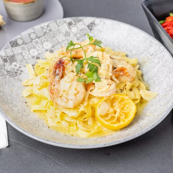 Creamy shrimp fettuccine pasta with parsley and a lemon half on a patterned plate.