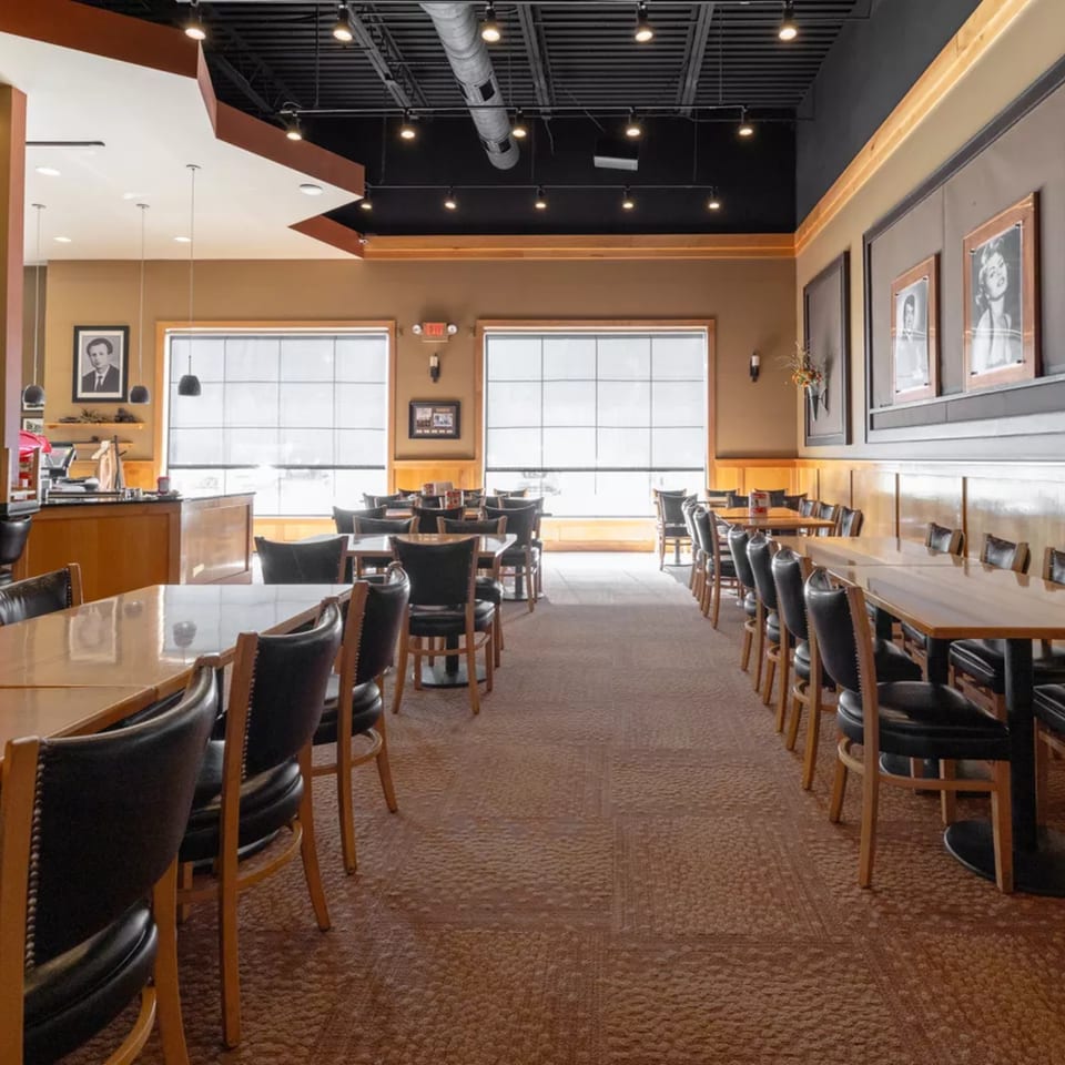 Interior of Vito's Coal Fired Pizza & Restaurant, showing empty dining tables with black chairs and large windows.