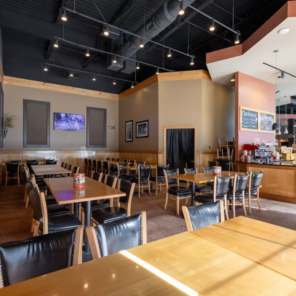 Interior of Vito's Coal Fired Pizza & Restaurant, showing dining tables, chairs, and a counter area.
