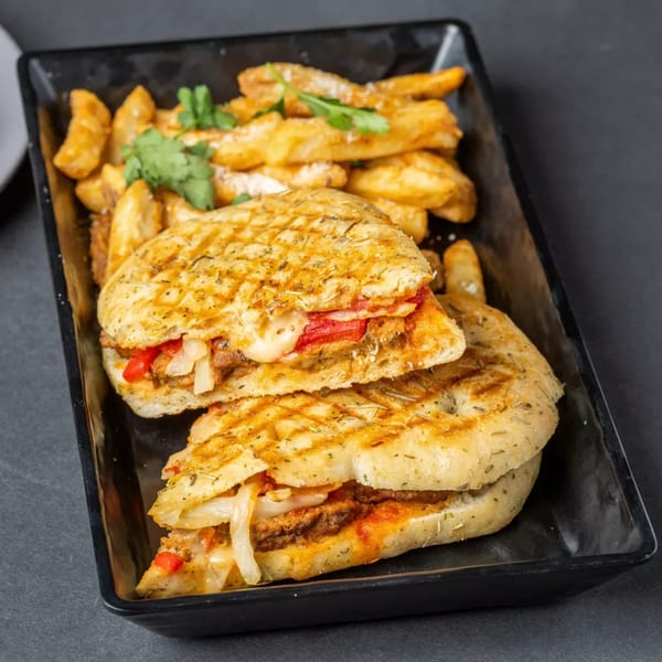 Grilled panini sandwich with melted cheese, peppers, and onions, served with seasoned potato wedges.