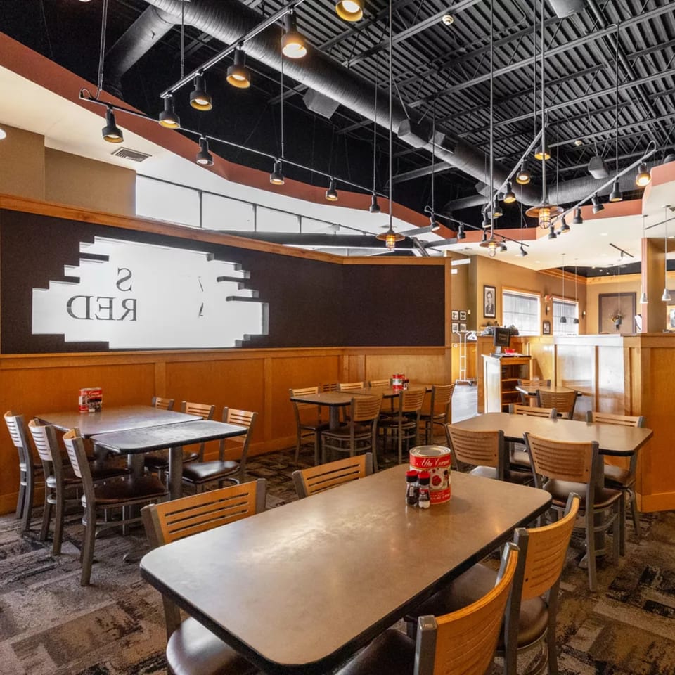 Interior of Vito's Coal Fired Pizza & Restaurant with empty tables, chairs, and exposed ceiling ducts.