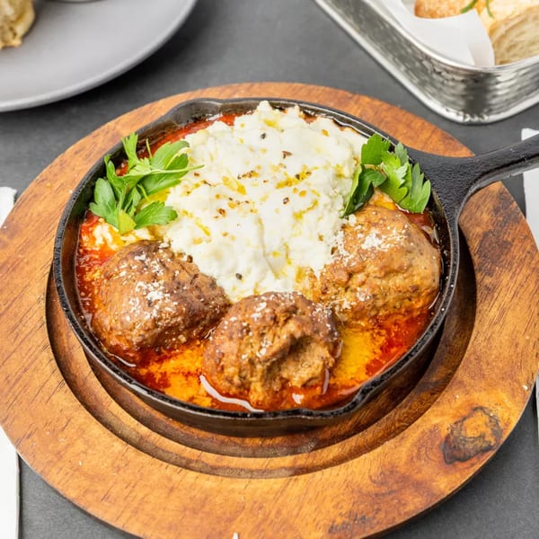 Meatballs in red sauce with a dollop of mashed potatoes and parsley in a cast iron skillet.