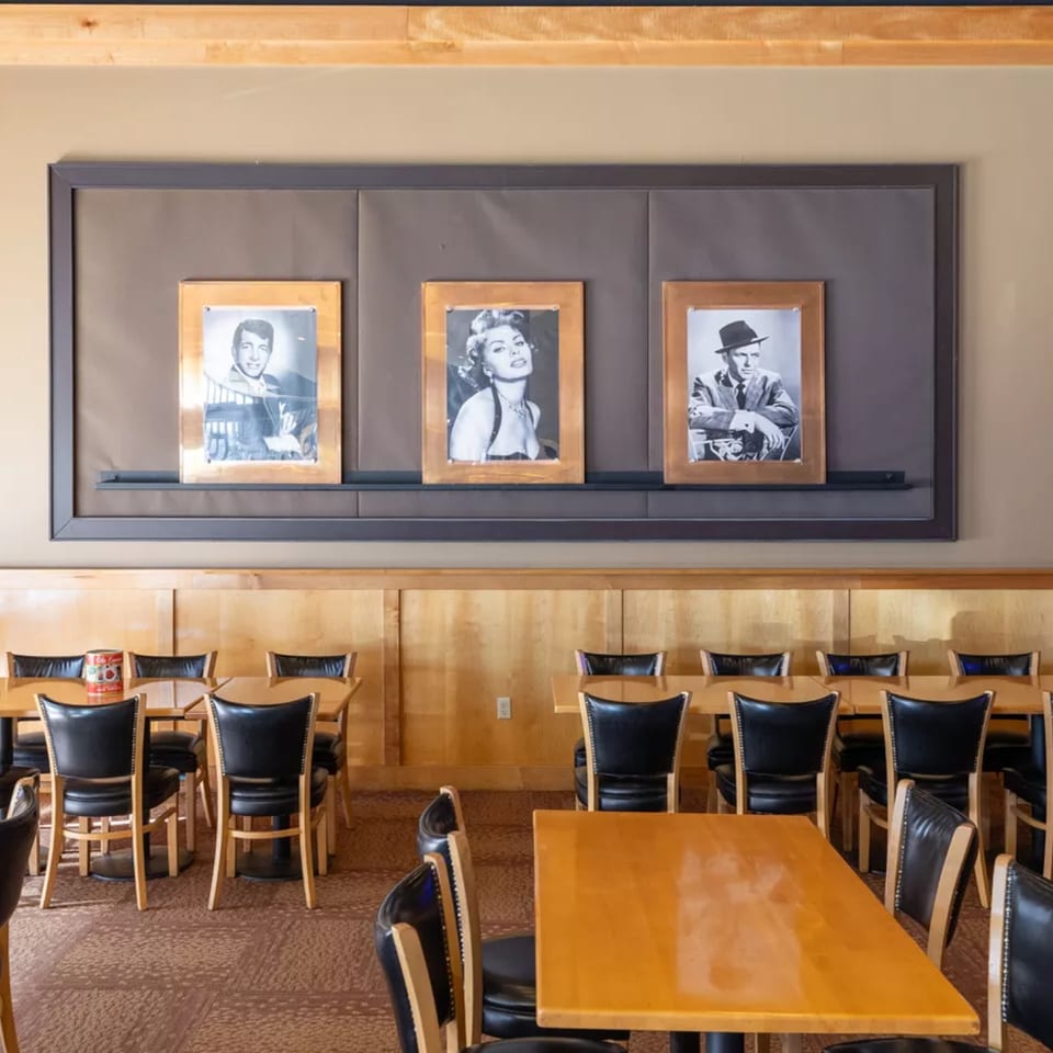 Vito's dining room with wooden tables, black chairs, and framed black and white celebrity photos.
